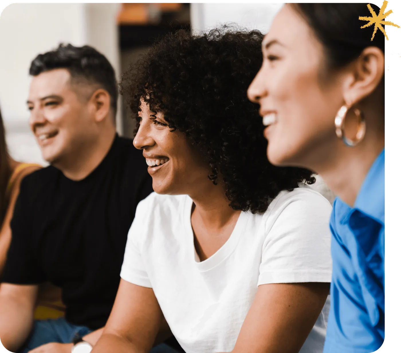 Brand photography from the relaunched Next Shift Learning identity — three colleagues seated together, laughing, with a small gold starburst mark in the corner.