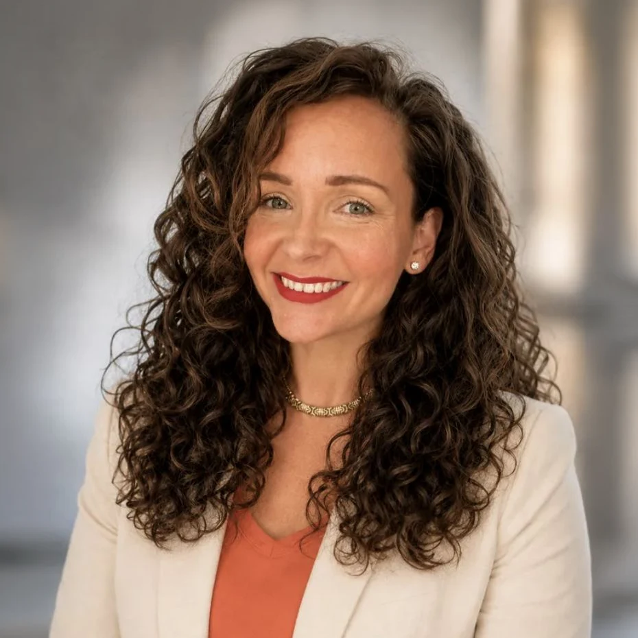 Ruth Dickson Eddy, smiling, with long curly hair, in a cream blazer over an orange top.